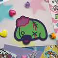 Zombie dog sticker in dog head shape, green with pink puff on head
